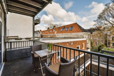 Fotoğrafın sol tarafında sandalyeler, masalar ve bir masa olan bir balkon arka planda bir apartman binasıdır.