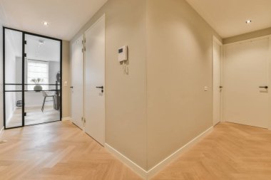 Ahşap zemini ve beyaz duvarları olan boş bir oda. Odanın sol tarafına açılan bir kapı var.