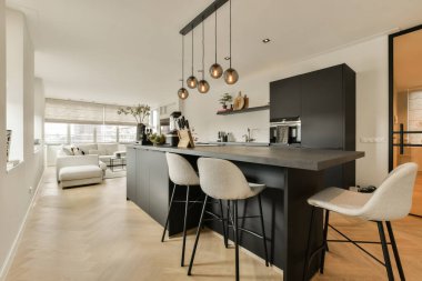 Beyaz duvarları, ahşap döşemeleri ve adada siyah dolapları olan modern bir dairede mutfak ve yemek odası.