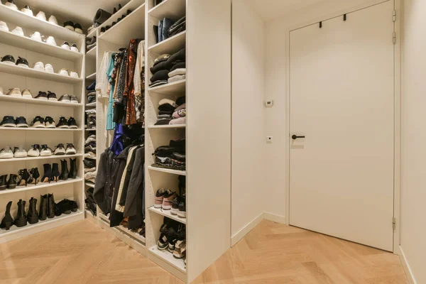 stock image a walk - in closet with wooden flooring and white shelves filled with various pairs of shoes, handbags and bags