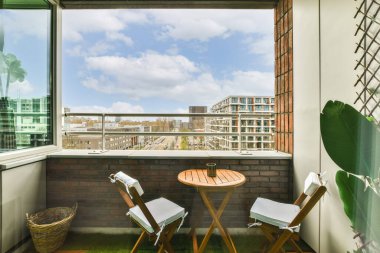 İki sandalyeli bir balkon ve açık bir pencerenin önünde bir masa.