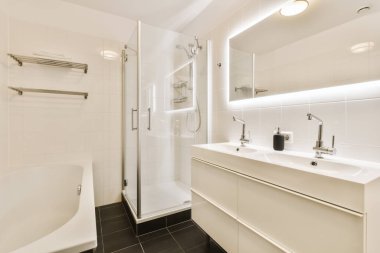 Modern bir banyo. Duvarlarında siyah fayanslar ve beyaz fayanslar var. Serbest duş da cabası.