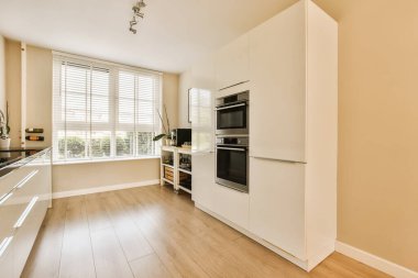 Beyaz dolapları ve siyah aletleri olan bir mutfak tezgahın üstünde fırının önünde, lavabo ve bulaşık makinesi.