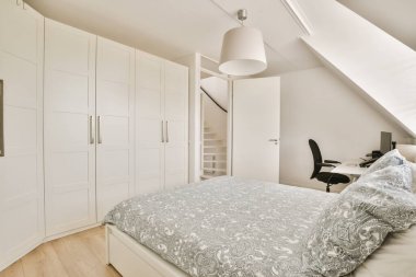 Yanındaki duvarda yatak odası, masa ve dolaplar olan beyaz bir dolap.