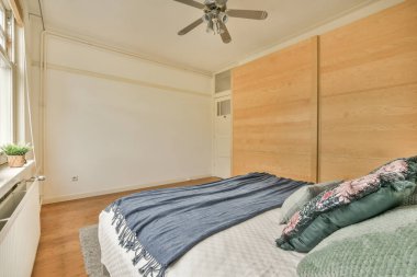 Yatak odasının duvarlarında ahşap paneller ve yatak başlığının üstünde tavan vantilatörü var.