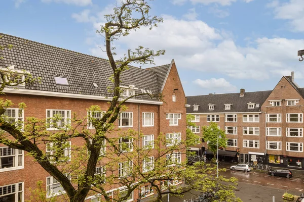 Kentsel bir bölgenin ortasındaki bazı binalar ve ağaçlar. Arabalar caddelerde yan yana park edilmiş.