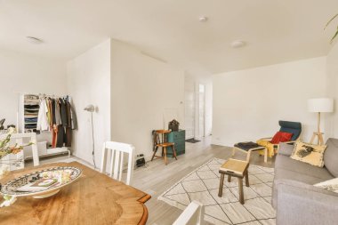 Beyaz duvarları ve odasının ortasında ahşap döşemeleri olan bir oturma odası yemek masası, iki sandalye ve bir...