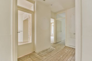 Ahşap döşeme ve duvarlarında beyaz boya olan boş bir oda. Köşesinde büyük bir ayna var.