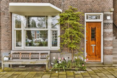 a brick house with a bench and flowers in the front yard, as seen from the side window on a sunny day