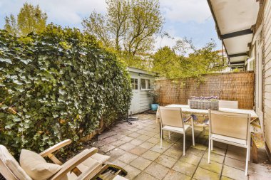 a patio with some chairs and plants in the back yard on a blue sky day, taken from an angleers perspective