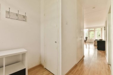 a hallway with white walls and wood flooring on the right side, there is an open door that leads to another room