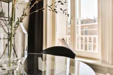 a vase with flowers in it on a table next to a window and a book sitting on top of the glass