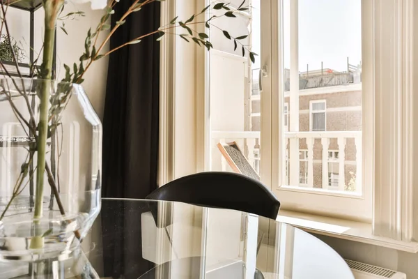 a vase with flowers in it on a table next to a window and a book sitting on top of the glass