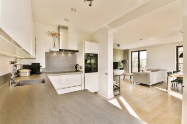 Beyaz duvarları, ahşap döşemeleri ve paslanmaz çelik aletleri olan bir ev ya da dairede mutfak ve oturma odası.