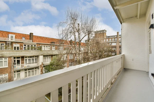 Önünde beyaz korkuluklar ve ağaçlar olan bir balkon, ön taraftaki apartmanlardan alınmış.