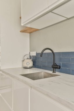 Beyaz dolaplı bir mutfak ve arkasında mavi metro fayansları olan bir lavabo var.