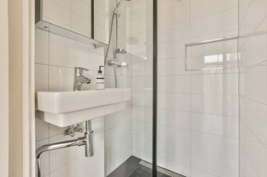 Duş kabininin kapısında beyaz fayansları ve siyah rendelenmiş döşemeleri olan modern bir banyo sağ tarafta açık.