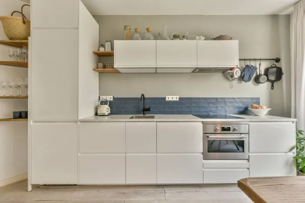 a kitchen with white cabinets and blue tiles on the wall behind it is an oven, dishwasher, toaster, sink