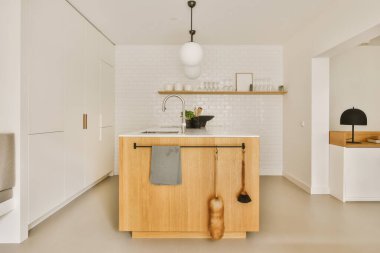 Duvarında beyaz fayanslar ve köşesinde ahşap dolaplar olan bir mutfak, lavabonun yanında.