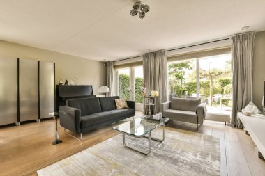 Oturma odası, koltuklar, sandalyeler ve terasa açılan cam kapının önünde bir sehpa.