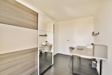 Odanın köşesinde masa, sandalye ve duvara monte edilmiş televizyon olan bir oda çok beyaz renklidir.