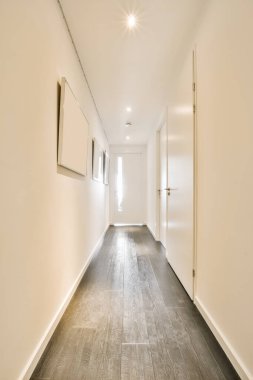 Koridordaki duvarda ahşap döşemeleri ve aydınlatma armaklarıyla boş beyaz bir oda aydınlatılıyor.