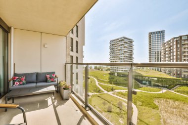 Dışında sandalyeler ve koltuklar olan bir balkon, sağdaki bazı binalara bakıyor.