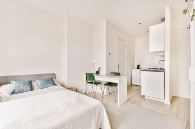 Yatak odası, masa ve yatağın yanındaki küçük mutfakta beyaz bir buzdolabı var.