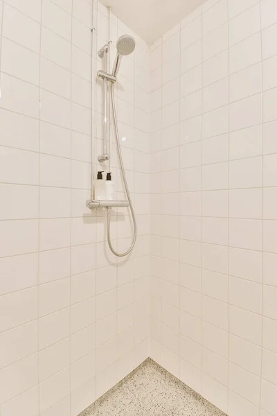 壁に接続されているシャワーアームで握られたシャワーヘッドと手の白いタイル付きのバスルーム — ストック写真