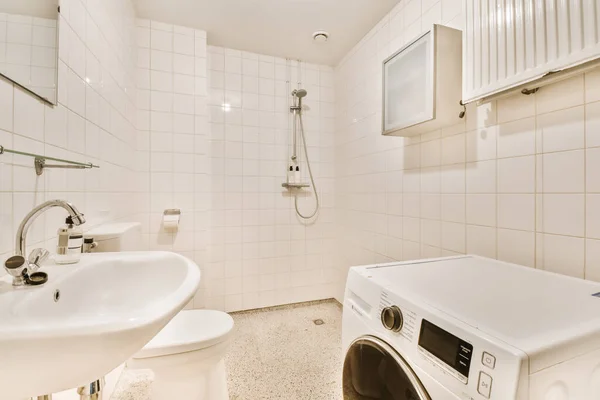 シンクの前の床に洗濯機と乾燥機が付いている小さなバスルームは白いタイルです — ストック写真