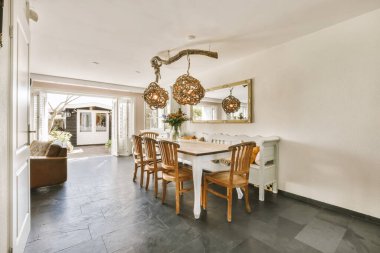 Beyaz duvarları ve yerde siyah döşemeleri olan bir yemek odası. Masanın üzerinde asılı büyük bir ayna var.