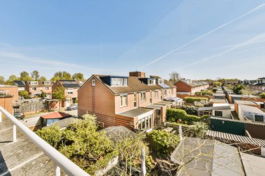 Güneşli bir günde bazı evler mavi gökyüzü ve arka planda beyaz bulutlar, bir apartman balkonundan görüldüğü gibi