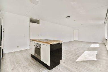 Beyaz duvarları, ahşap döşemeleri ve adada siyah aletleri olan yeni bir dairede boş bir mutfak ve yemek odası.