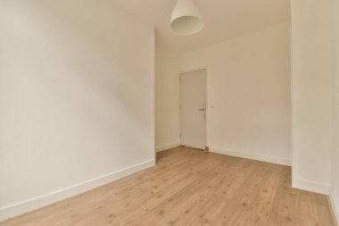 Beyaz duvarları ve ahşap döşemeleri olan boş bir oda. Duvardaki lamba armatürünü ortaya çıkarmak için kapı açık.