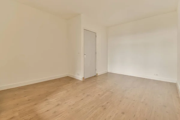 一间有木地板和白墙的空房间 有一扇通向房间左边的门 — 图库照片