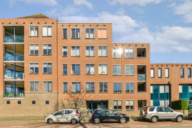 Önünde arabaların park ettiği bir apartman ve caddenin karşısındaki mavi gökyüzü.