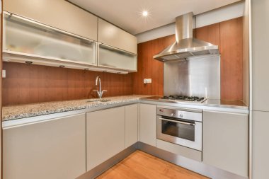 Tezgahın üzerinde beyaz dolaplar ve paslanmaz aletler olan modern bir mutfak, yukarıdan çekilmiş bir daire içi fotoğraf.