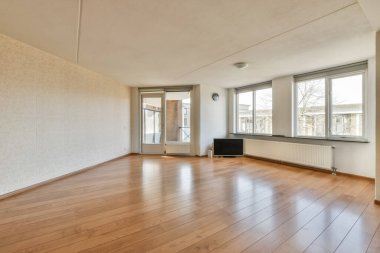 Boş bir oturma odası, ahşap döşeme ve evin önündeki sokağa bakan büyük pencereli.