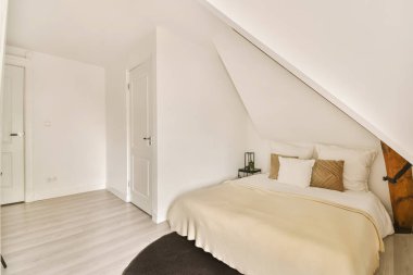 Tavan arasında beyaz duvarları ve ahşap döşemeleri olan bir yatak odası.