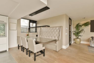 Beyaz sandalyeli bir yemek odası ve odanın ortasında büyük bir bitki odası açık bir mutfak alanıdır.