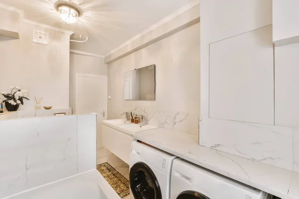 壁に白い大理石のタイルの洗濯機 乾燥機および洗濯機が付いている洗濯室は上の大きい鏡があります — ストック写真