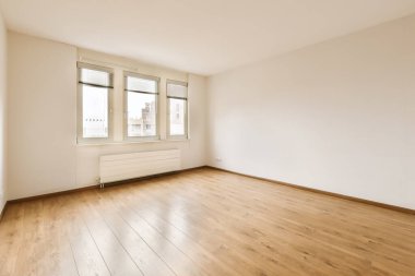 Ahşap döşeme ve duvarlarında beyaz boya olan boş bir oda. Köşesinde büyük bir pencere var.