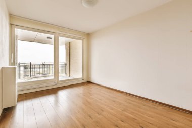 Ahşap döşemeli ve geniş pencereli boş bir oda balkondan denize kadar suya bakıyor.