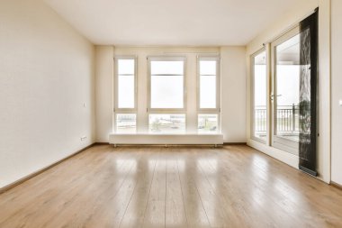 Boş bir oturma odası, ahşap zemin ve şehir manzarasına bakan geniş pencereli.