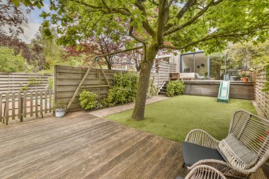 Bahçesinde ağaçlar, çalılar ve çiçeklerle çevrili ahşap süslemeli ve yeşil çimenli bir bahçe.