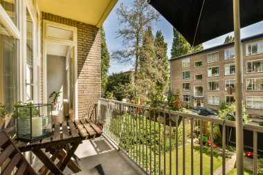 Masanın üzerinde şemsiyesi olan bir balkon ve bir tarafında iki sandalye var. Uzakta ağaçların görüntüsü var.