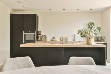 Adanın içinde siyah dolapları ve beyaz mermer tezgahları olan modern bir mutfak bir saksı dolusu bitkiyle çevrilidir.