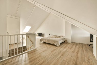 Tavan arasında ahşap döşemeli ve beyaz duvarlı bir yatak odası. İkinci kata çıkan merdiveni gösteriyor.