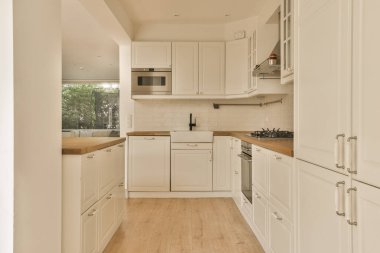 Beyaz dolapları ve ahşap tezgahları olan bir mutfak. Kapının önünde, odanın önünde.