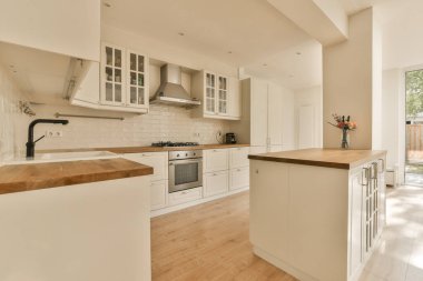 Bahçe kapısının önünde beyaz dolaplar ve ahşap tezgahlarla dolu bir mutfak.